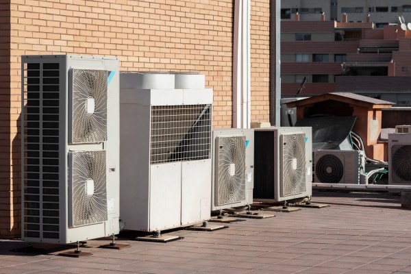 Multiple outdoor HVAC condenser units installed on a rooftop beside a brick building.