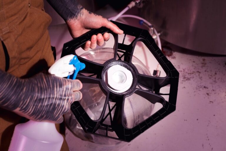 A Person spraying a liquid onto a black plastic wheel-like component over a metal container.