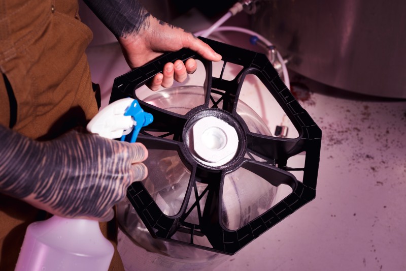 A Person spraying a liquid onto a black plastic wheel-like component over a metal container.